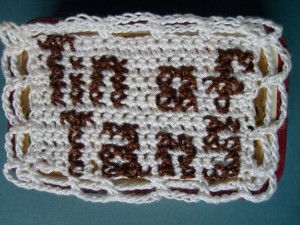 Crocheted and cross stitched cover of the Tin of Tans